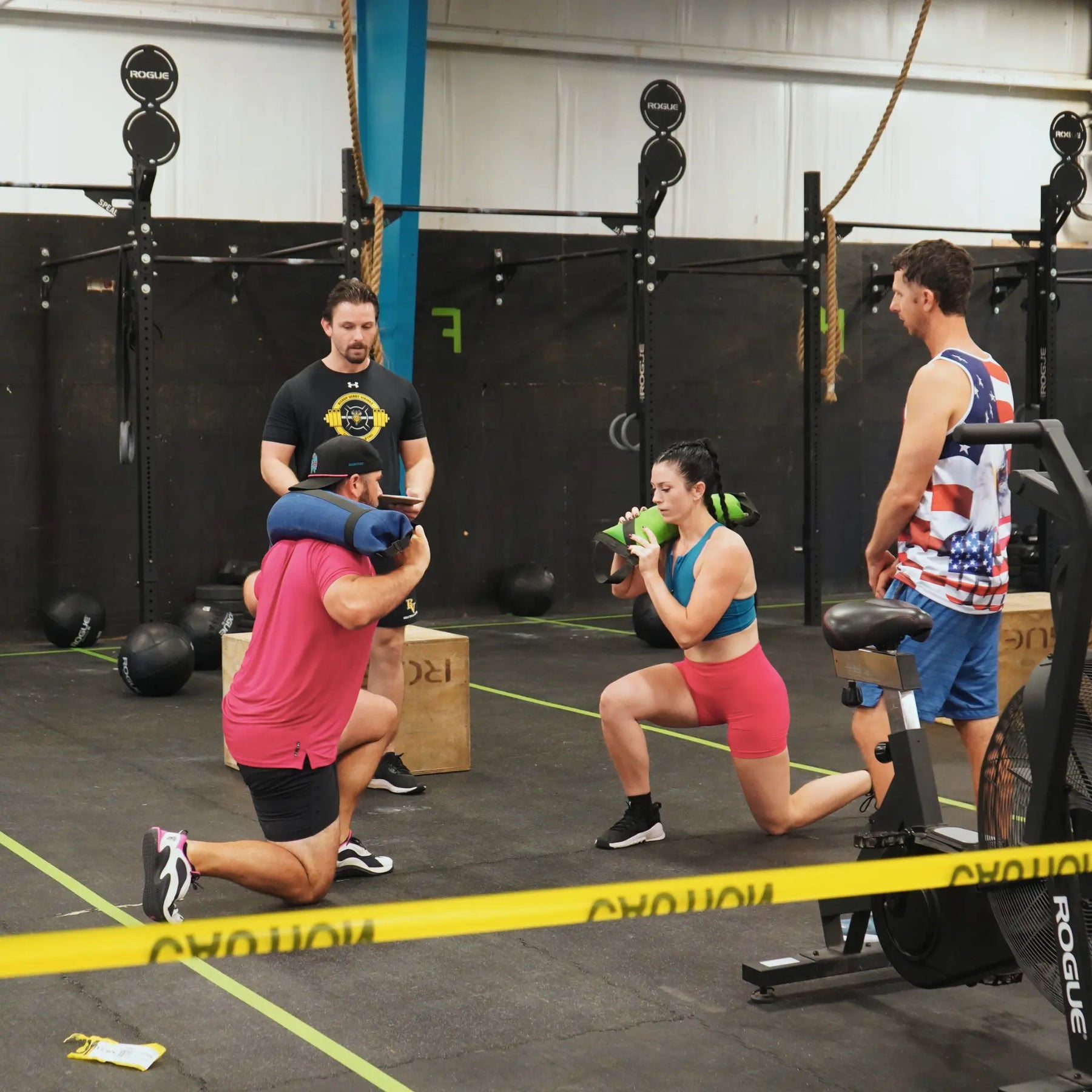 People performing lunges with weighted bags in a gym.
