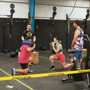 People performing lunges with weighted bags in a gym.