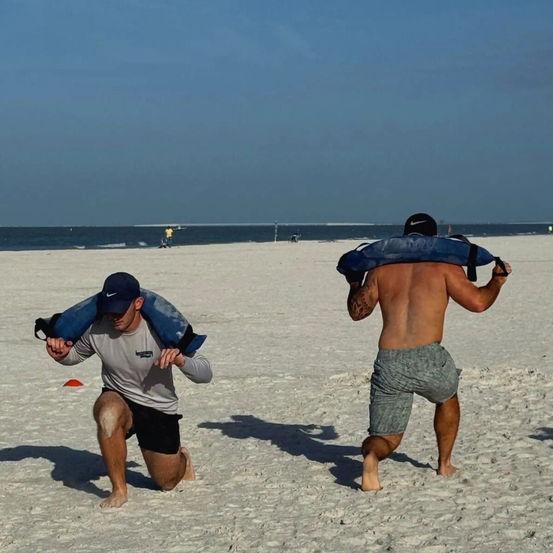 Men performing fitness exercises with weighted workout bags on a sandy beach