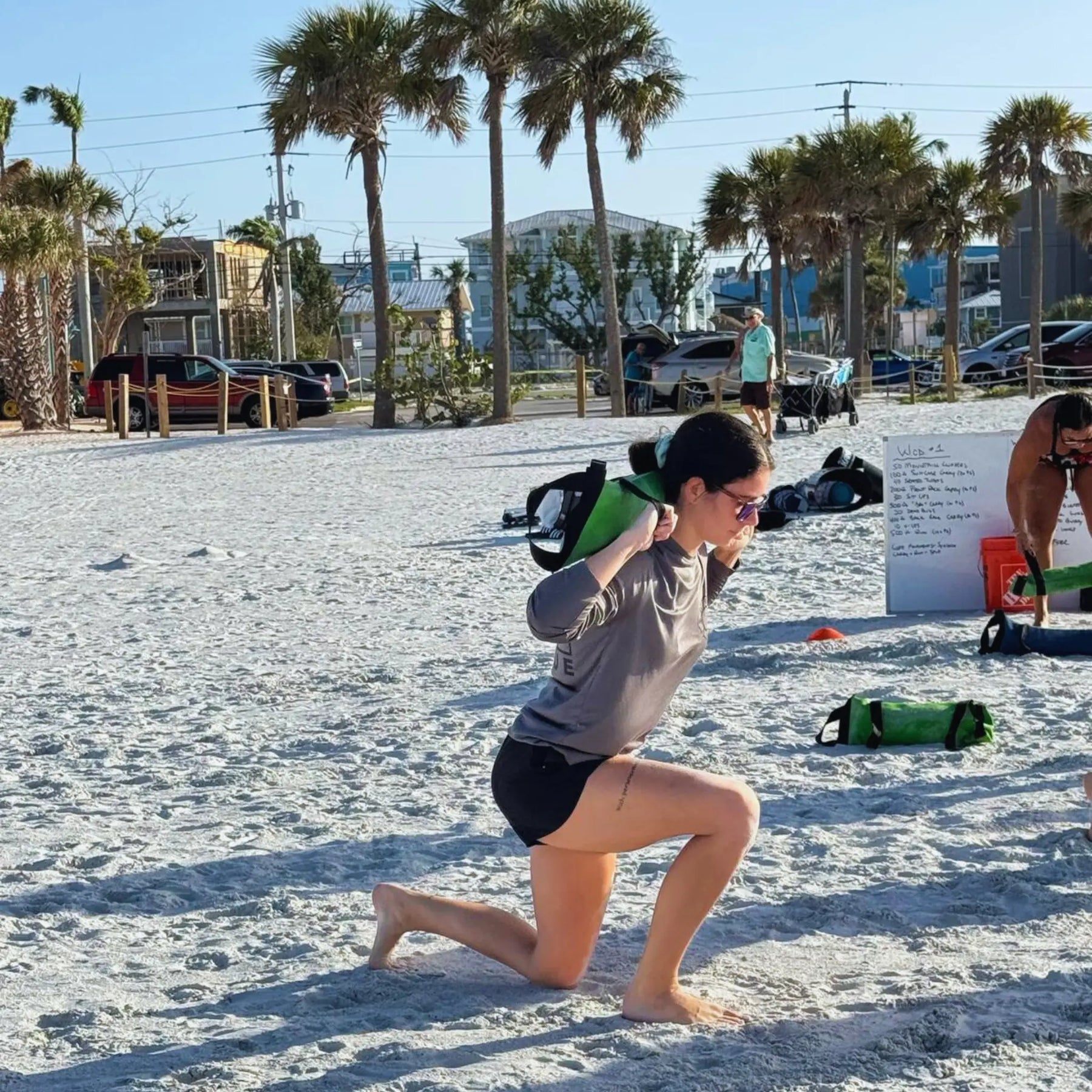 Woman lunging with a green workout bag on a beach
