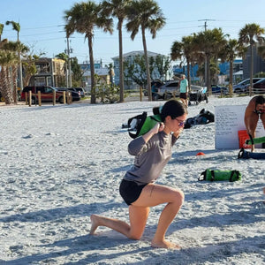 Woman lunging with a green workout bag on a beach