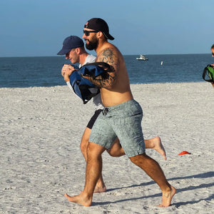 Two men performing a workout on a sandy beach with a workout battle bag.