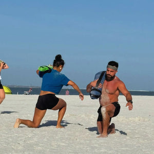 People doing lunges with workout battle bags on a sandy beach
