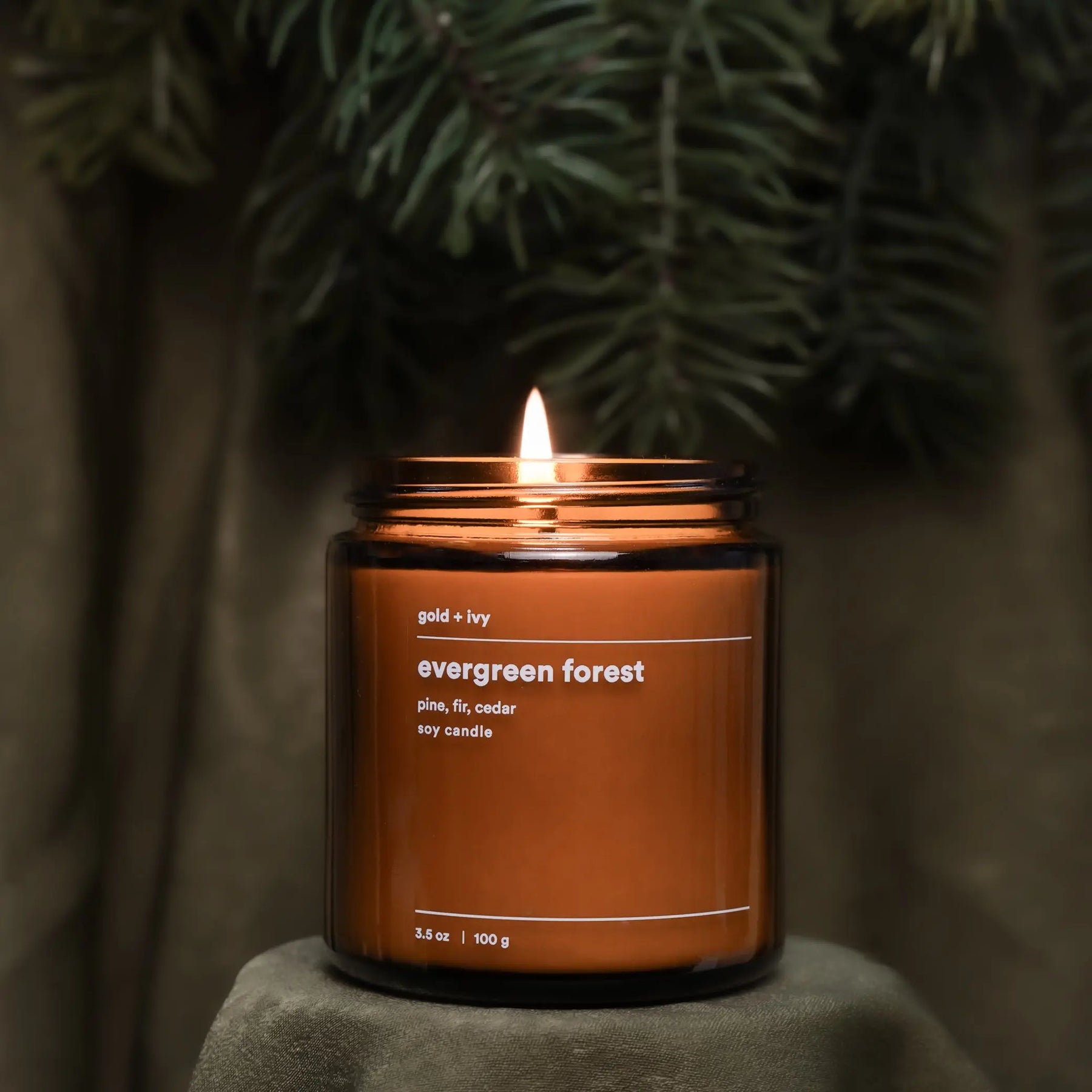 Brown glass soy candle labeled "Evergreen Forest" with a lit flame.