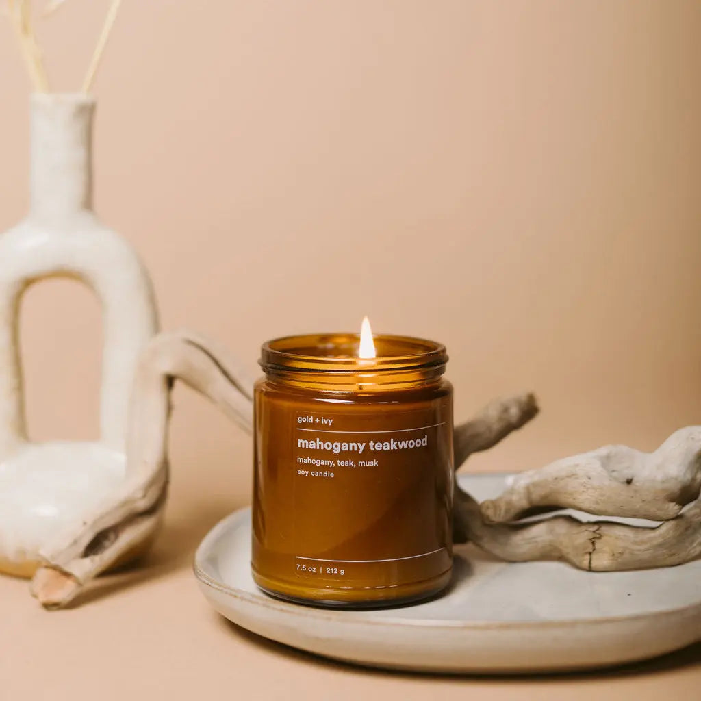 Amber glass mahogany teakwood candle with lit flame, driftwood, and vase.
