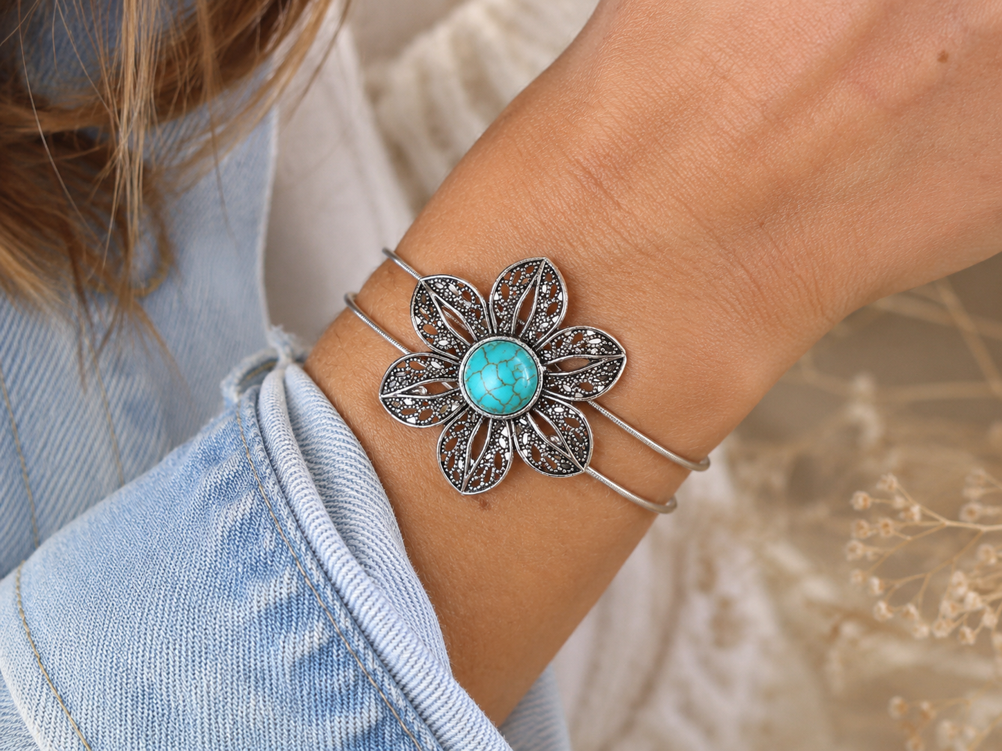Silver bracelet with a turquoise stone on a wrist, against a blurred natural background.